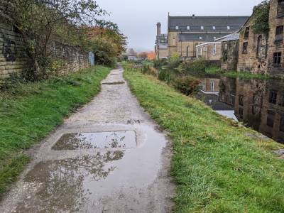 An uneven gravel path next to a grassy verge by the side of a canal