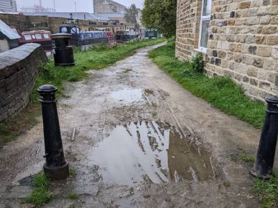 A muddy unnevan gravel path with small barriers either side, and canal boats in the distance
