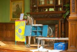 Part of an exhibition featuring a sign, a children's riding horse toy and shelves. More shelves and a portrait are in the background