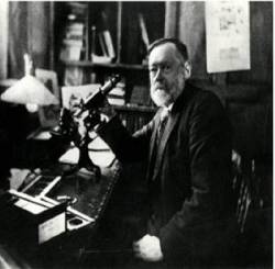James Lomax examining a specimen under a microscope at his desk, with various lab tools and papers nearby.