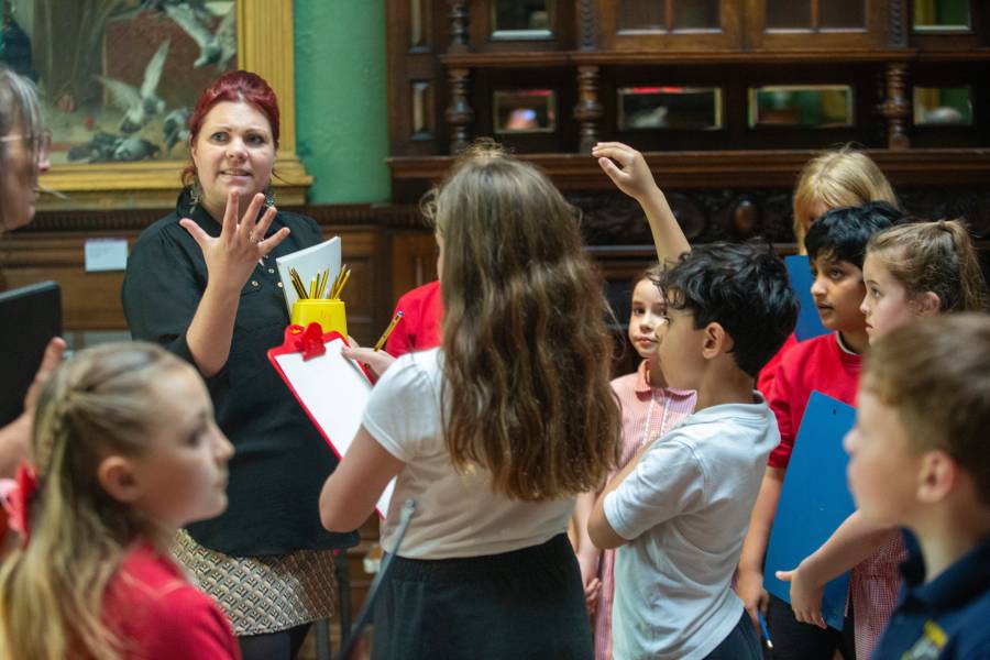 A woman engages with children in a brightly lit room, fostering a lively discussion among them.