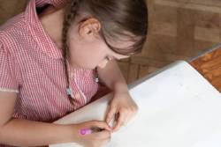 A young girl is focused on drawing with crayons on a piece of paper at a table