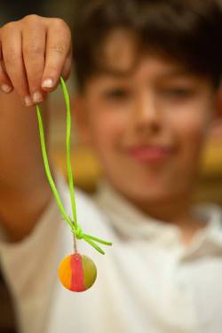 A young boy proudly holds up a vibrant, multicoloured string, showcasing its bright hues against a neutral background.