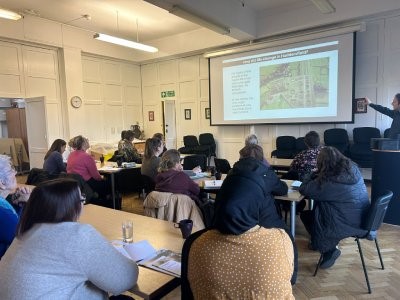A group of people seated in chairs, engaged in conversation about Roman life in a well-lit room.