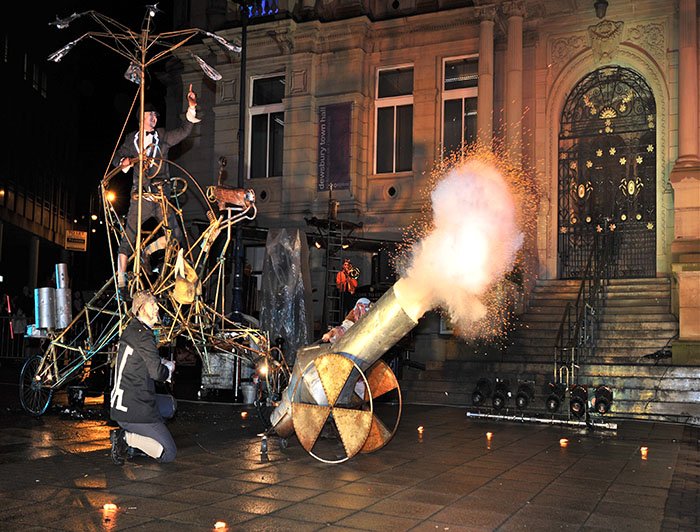 A bizarre vehicle with a cannon crosses in front of the town hall at night