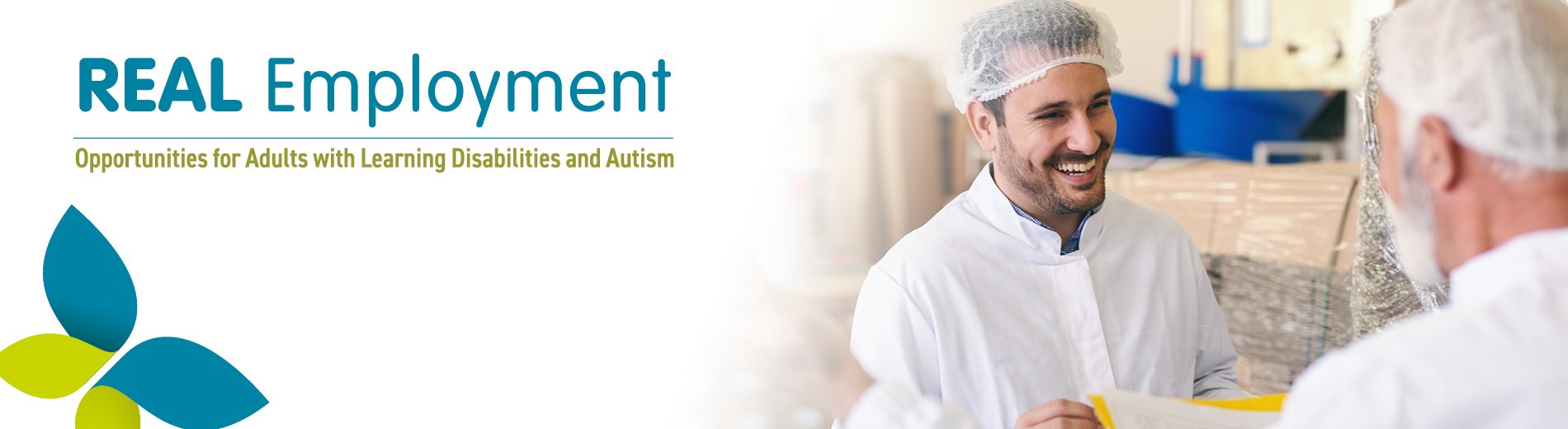 Two men talking in a factory, wearing white uniforms and hairnets. One is facing the camera and laughing