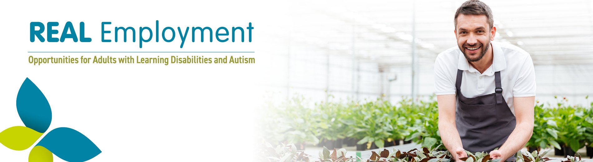 A smiling man wearing an apron and tending plants in a large greenhouse