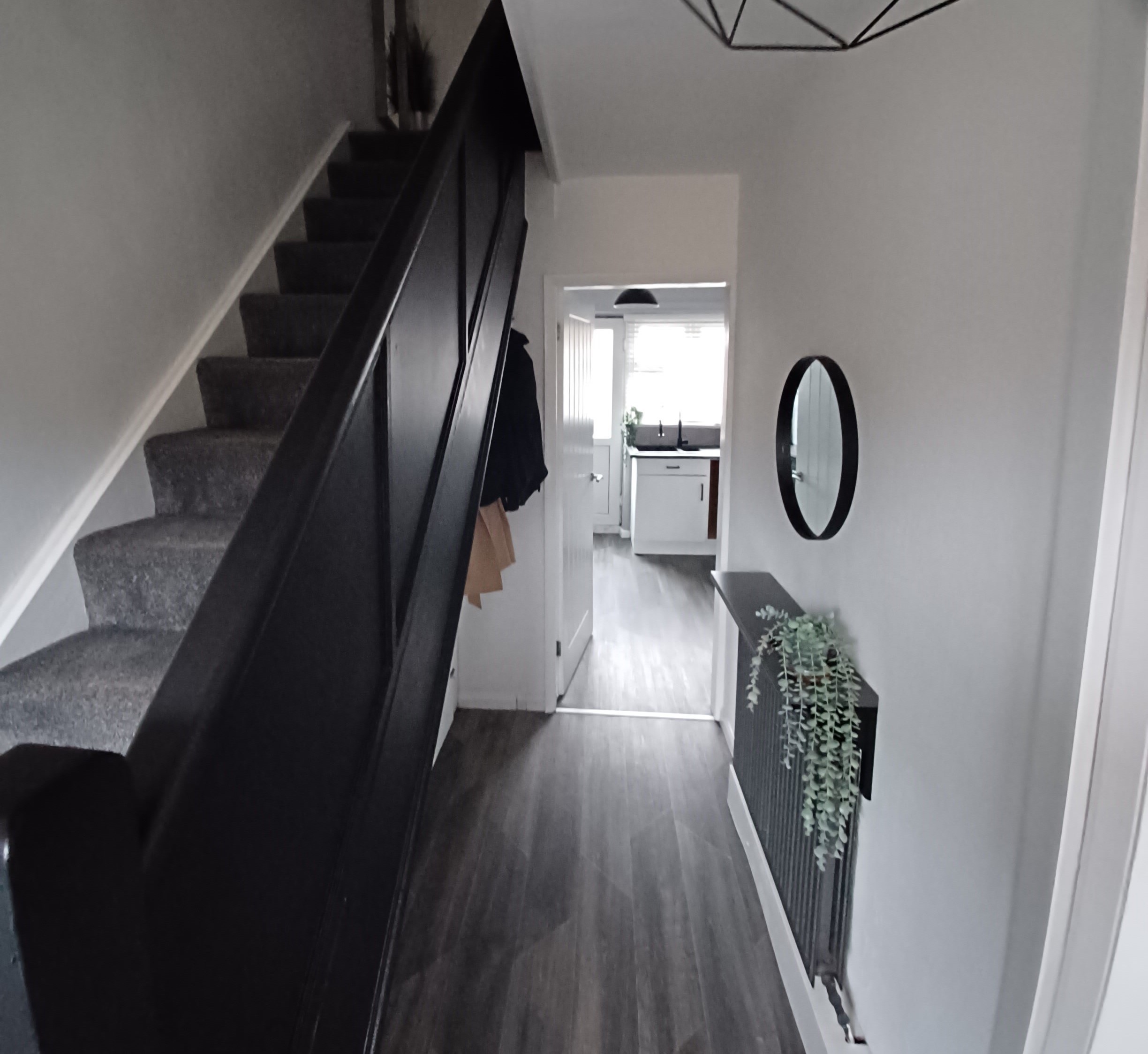 inside of a house lobby with stairs leading to the upper floor with black carpet and a doorway leading to a kitchen