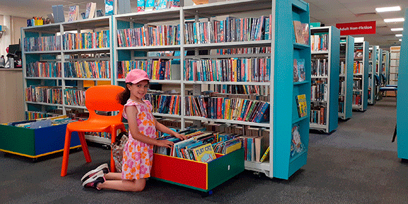 Young girl choosing books in the Children's Library section of a Kirklees Library Hub