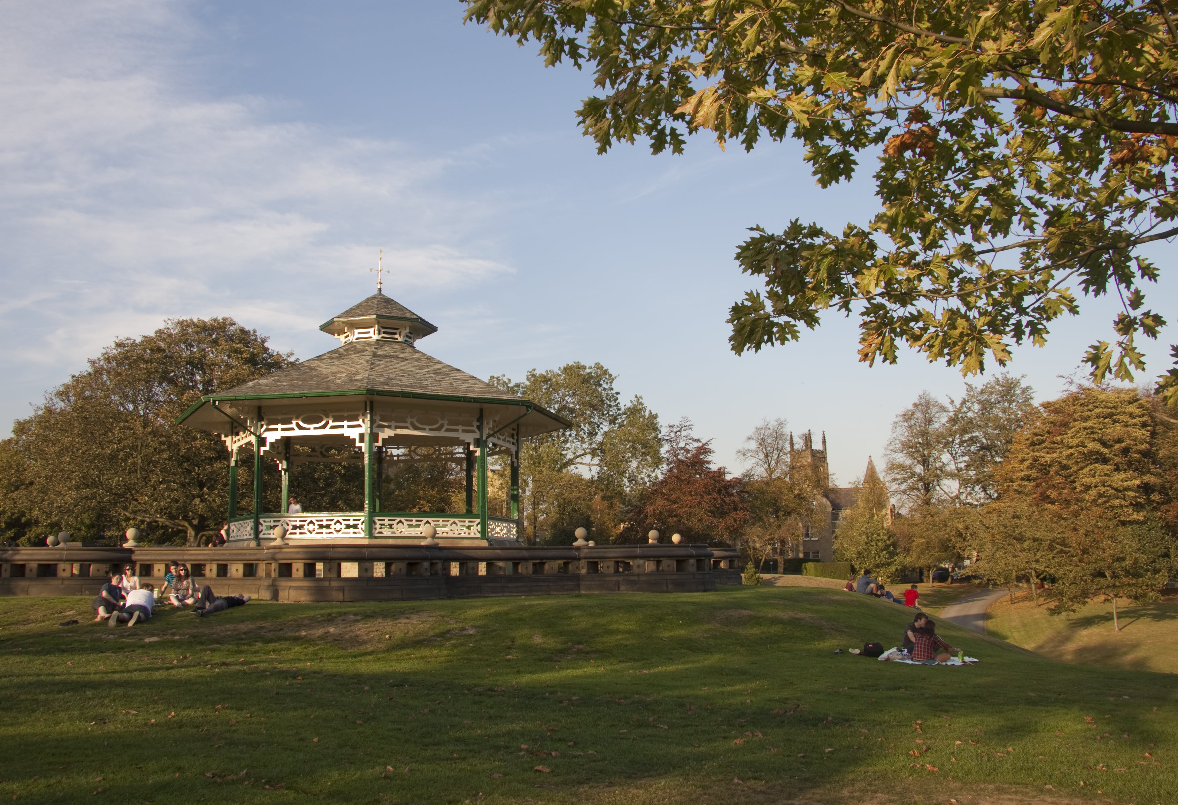 Band stage at a local park with people sat in groups on the grass.
