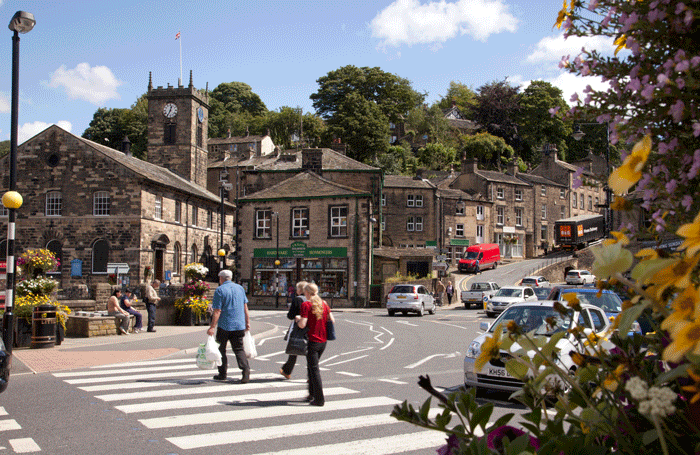 Pedestrians using a zebra crossing in Holmfirth, while a queue of traffic waits on a sunny day