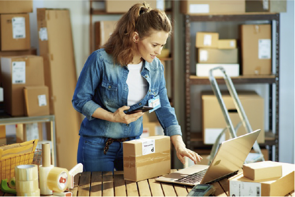 A woman packing orders and using a laptop