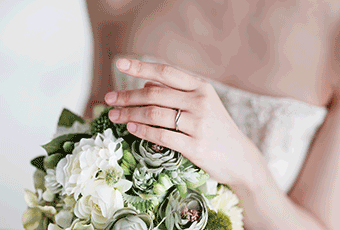 A person's hands with a ring on, holding wedding flowers 